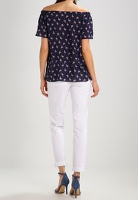 Marinblus med avskurna axlar och blommönster, matchad med vita byxor och blå klackskor. Slätt tyg, avslappnad passform, korta ärmar.