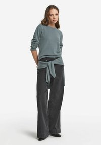 Jasnoniebieski sweter z kaszmiru, z długimi rękawami. Czarne szerokie dżinsy z węzłem na wysokości talii. Czarne buty na pointed toe.