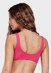 Bralette texturizado rosa con tirantes anchos y espalda redondeada. La tela presenta un patrón acanalado, proporcionando un ajuste ceñido y una cobertura mínima.