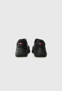 Zwarte sportschoenen met een gestructureerd mesh-lichaam en een solide rubberen zool. Heeft rode branding op de hiel en een slanke silhouet.