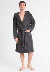 Grå terry badekåbe med hætte, frontlukning med bånd og to forlommer, der har en blød tekstur og et afslappet design.