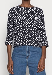 Tmavě modrý top s puntíky a tříčtvrtečními rukávy, kulatým výstřihem, vyrobený z měkkého materiálu, se bílými kruhovými vzory, volnější střih.