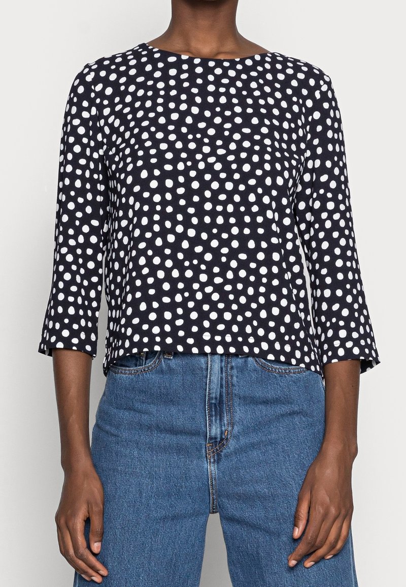 Tmavě modrý top s puntíky a tříčtvrtečními rukávy, kulatým výstřihem, vyrobený z měkkého materiálu, se bílými kruhovými vzory, volnější střih.
