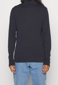 Navyfarbener Rollkragenpullover aus weichem, geripptem Material mit langen Ärmeln und körperbetontem Design, kombiniert mit hellblauen Jeans.