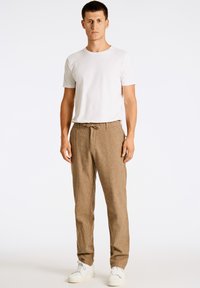 Lätta bruna linbyxor med dragsko i midjan, tillsammans med en åtsittande vit t-shirt i bomull och vita sneakers.