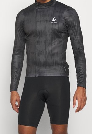 Atleet draagt een nauwsluitend zwart langermig fietsjersey met subtiel patroon en zwarte gewatteerde fietsbroek.