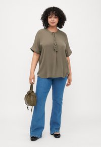 Olive green blouse with rolled sleeves and front tie detail, paired with blue flared jeans and a small olive bag. Smooth fabric texture.