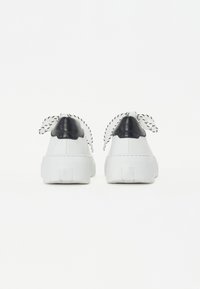 Sneakers bianchi con suola testurizzata, dettagli neri sul tallone e lacci a strisce bianche e nere. Materiale liscio con design arrotondato.