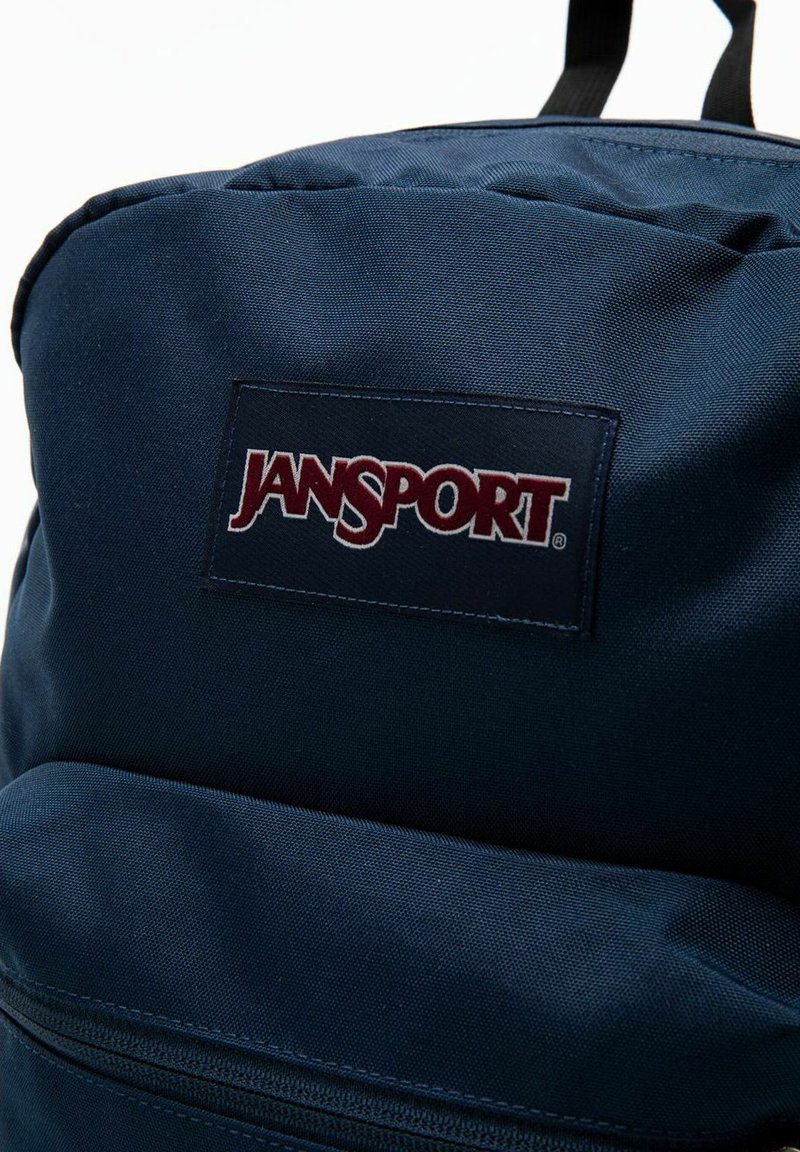 Zaino Jansport blu navy realizzato in tessuto resistente, caratterizzato da un logo in evidenza e una tasca frontale con zip per riporre gli oggetti.