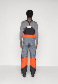 Suksiülikond, millel on reguleeritavad mustad rihmad, halli, oranži ja tumesinise värvi blokiseerimise disain. Veekindel materjal ja lukud.