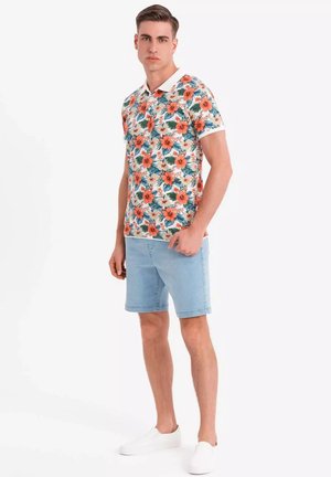 Blommig polo i vitt med orange och teal mönster, kombinerat med ljusblå jeansshorts och vita slip-on skor.