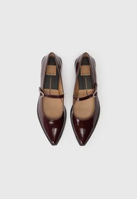 Bailarinas de charol burdeos con punta afilada, tirante estilo Mary Jane y detalle de hebilla plateada, que presentan un acabado suave y un tacón bajo.
