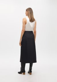 Vitt ärmlöst linne ihop med en mörk kjol som når knäna. Modellen har svarta knähöga stövlar med klack. En enkel, modern stil.