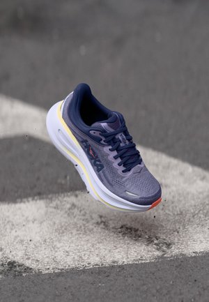 Chaussure de course avec une tige en mesh gris, des accents bleu marine, une semelle intermédiaire jaune et une semelle extérieure blanche. Comprend un design à lacets et des détails de logo.