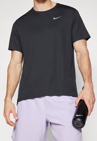 Camiseta negra de Nike de manga corta con cuello redondo, que presenta un logo reflectante de Nike en el pecho. La tela tiene una textura suave.