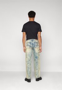 Lys blå, lett slitte denimjeans med baklommer og avslappet passform. Brukt med en svart t-skjorte med korte ermer og svarte sko.