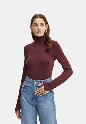 Maglione a maniche lunghe color bordeaux con collo a imbuto realizzato in tessuto elastico, caratterizzato da un design aderente e maniche lunghe con dettagli a bottoni. Indossato con jeans a vita alta.