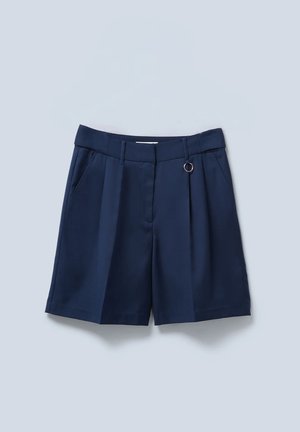 Shorts bleu marine en tissu léger, avec des plis, des poches latérales et un accent en métal sur la ceinture.