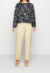 Blusa nera a fiori con maniche lunghe e scollo rotondo, abbinata a pantaloni larghi color crema e scarpe con tacco nude.