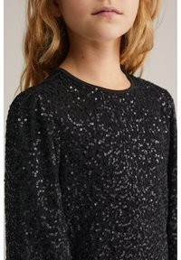 Melna garām piedurknēm augšdaļa, rotāta ar spīdumiem savirpinātā rakstā, ar apļveida izgriezumu un mīkstu, teksturētu audumu.