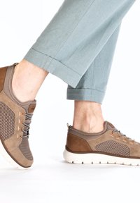 Baskets brunes en matières maillées et en daim, avec des lacets et des accents gris, une semelle blanche rembourrée et des détails de couture visibles.