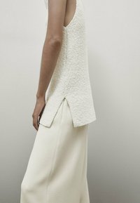 Haut sans manches texturé blanc avec une fente dans le dos, associé à un pantalon large blanc, les deux en tissu doux et lisse.