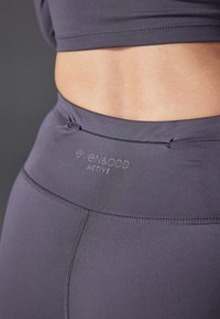 Donkergrijze sportlegging met een hoge tailleband, gestikte details en een subtiele merklogo bij de taille. Glad, rekbaar materiaal.