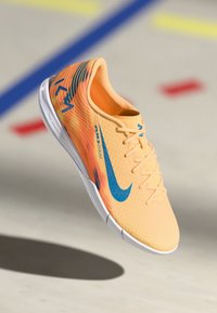 Nike spordijalatsid, millel on kerge oranž ülemine osa siniste detailidega, tekstuuriga muster, paelaga sulgemine ja valge soe.