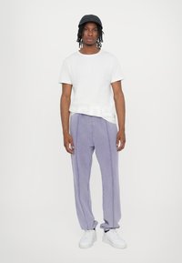 White short-sleeve t-shirt with a printed hem, paired with lavender loose-fit pants featuring contrasting stitching. Complete with white sneakers.