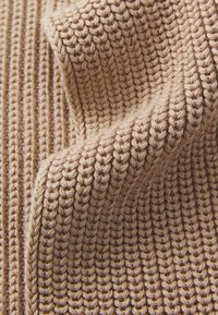 Tessuto lavorato a maglia beige con un motivo testurizzato a coste. Il materiale appare spesso e accogliente, mostrando filato morbido e ritorto.