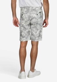 Graue Shorts mit weißem tropischem Blättermuster, Gesäßtaschen und Gürtelschlaufen; kombiniert mit weißen Turnschuhen auf einem schlichten Hintergrund.