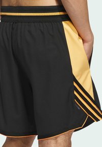 Pantalones cortos de entrenamiento negros con un panel lateral amarillo, que presentan acentos en naranja. Están hechos de un material suave y ligero con una cinturilla transpirable.