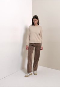 Beige gebreide trui gecombineerd met bruine corduroy broek, met een losse pasvorm en een gestructureerde stof. Sneakers met lichte en donkere accenten.