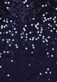 Marinefarbener Stoff, verziert mit verstreuten, glänzenden Pailletten in Silber und Schwarz, die eine strukturierte und reflektierende Oberfläche bilden.