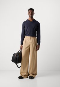 Jersey de marina con cuello ancho, pantalones de tela beige con pliegues, bolso de piel negro con asas marrones y zapatos negros. Diseño simple y estructurado.