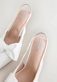Valged satiinist slingback-sandaalid, mille esiosas on kaunistused siidiste nööridega. Siledast nahast sisetald ning metalliline aktsent kanna peal.