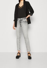 Šedé džíny s úzkým střihem, zkombinované s černým tílkem s krajkovým lemem a černým sakem. Hluboké lodičky na vysokém podpatku dodávají kontrast.