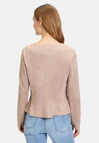 Ljusbeige mockajacka med långa ärmar, figursydd silhuett och utställd fåll. Bärs med ljusblå denimjeans, minimal synlig detaljer.