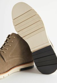 Scarpe in suede marrone con una texture liscia, caratterizzate da una robusta soletta in gomma; cuciture dettagliate e una sezione di trazione nera a contrasto.