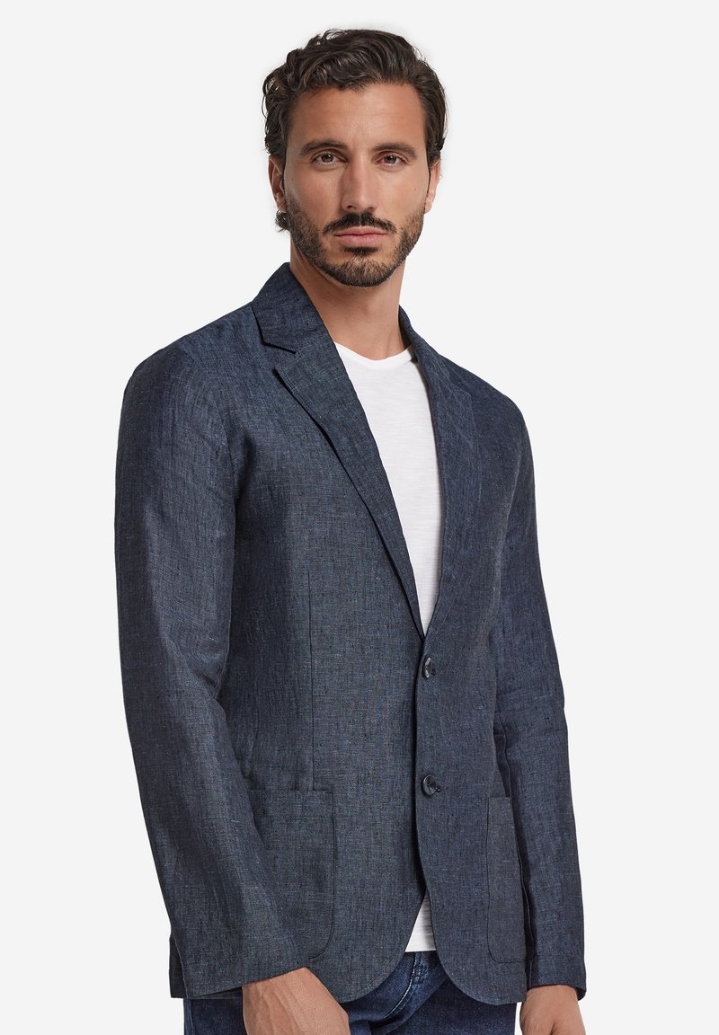 Granatowy lniany blezer z wyciętym kołnierzem, dwoma guzikami i dwoma przednimi kieszeniami. Gładka tekstura i dopasowany krój. Noszony na białej koszuli.