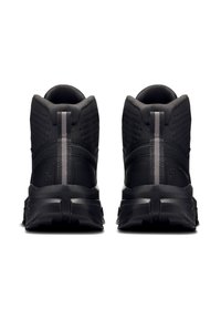 Paar schwarze Sportschuhe mit hoher Knöchelstütze, strukturiertem Stoff, dicken Sohlen und reflektierenden vertikalen Streifen an der Rückseite.