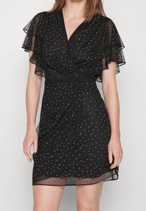 Vestido negro con mangas cortas de organza superpuestas, con un diseño cruzado, adornado con tachuelas plateadas y un detalle de cintura fruncida.