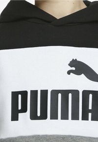 Sudadera en blanco y negro hecha de tela suave. Presenta un gran logotipo "PUMA" y un gráfico de un puma saltando. Incluye un panel inferior en gris.