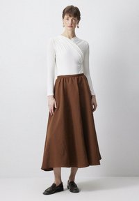 Lange bruine rok met een geraffineerde taille, gecombineerd met een witte top met lange mouwen en een gewikkeld ontwerp. Soepele textuur, minimalistische stijl.