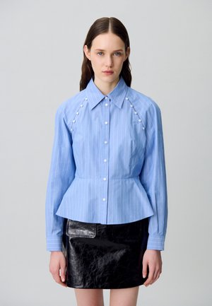 Camisa de botones a rayas azules con cintura peplum, con botones blancos y mangas raglán. Combinada con una minifalda de cuero negra.