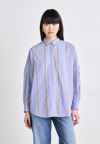 Light blue button-up shirt with vertical orange and cream stripes. Loose fit, wide sleeves, and a classic collar. Paired with light denim jeans.