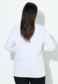 Witte lange mouwen shirt van katoen. Heeft een ronde halslijn en een losse pasvorm. De achterkant toont een gladde stof en een rechte zoom.