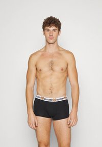 Fekete boxeralsó fehér derékpánttal, amely maci mintával díszített, puha anyagból, a modell semleges kifejezéssel áll.