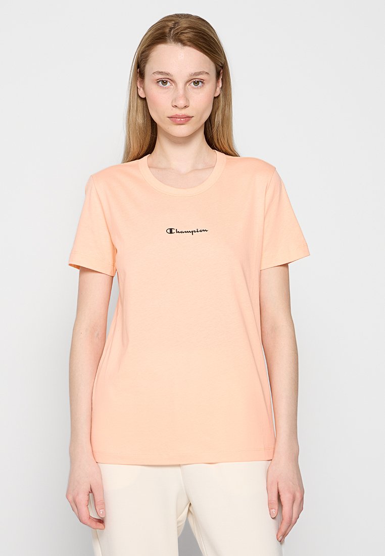 T-shirt di cotone pesca con scollo rotondo e maniche corte. Presenta un piccolo logo "Champion" nero centrato sul petto.