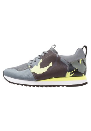 Lavtsiddende atletiksneaker i grå med gul og grøn camouflage-mønster, hvid mellemsål, sort ydersål og trækflig på hælen.